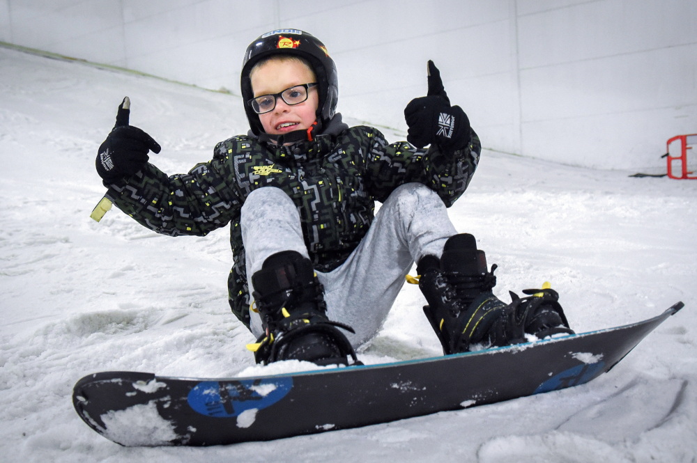 A young male child snowboarding on the slopes in the snowdome